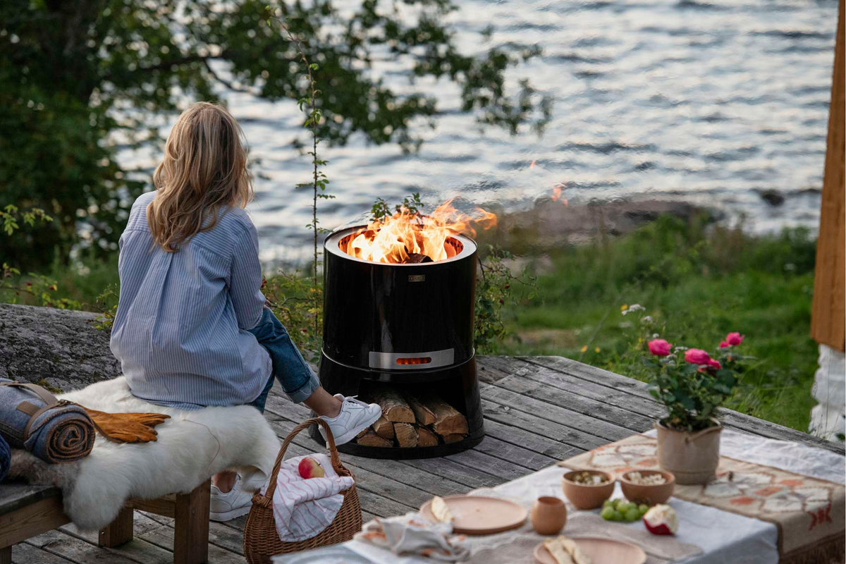 Person sitting by a fire pit by a lake with a scenic view.
