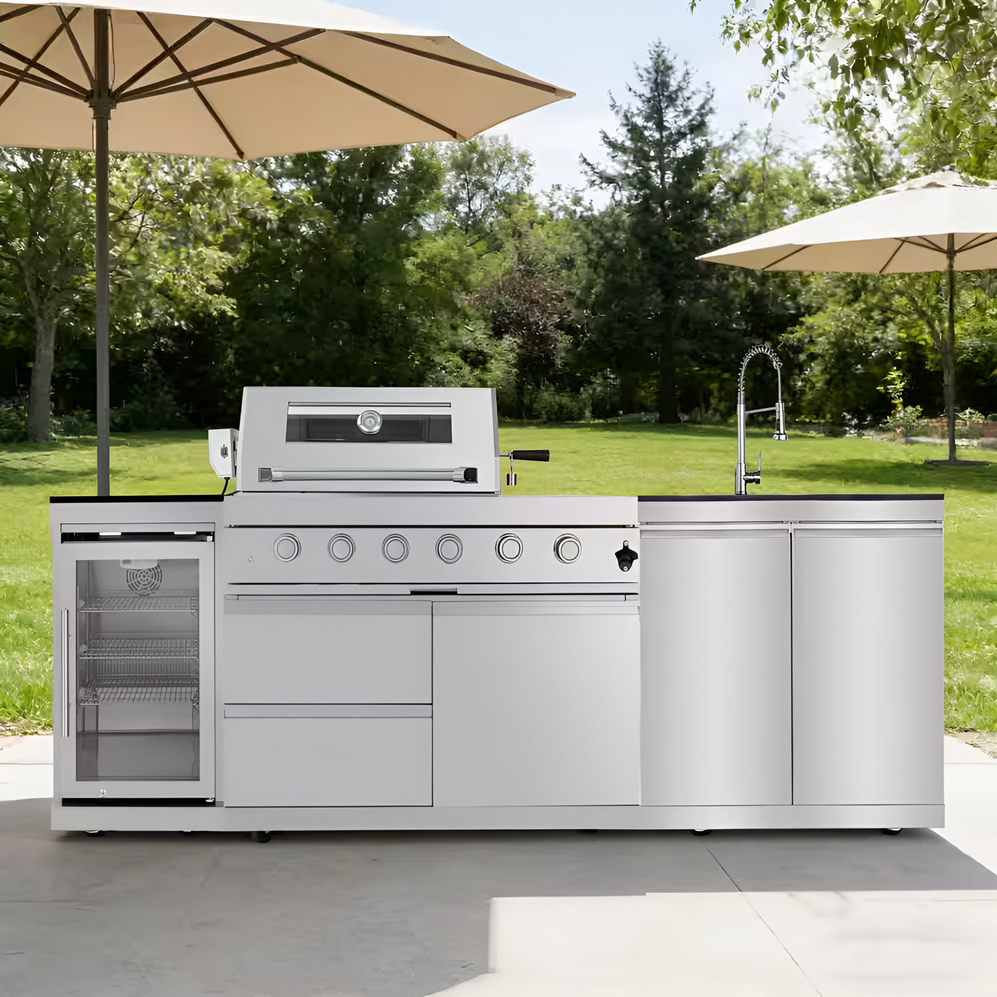 Outdoor kitchen with stainless steel grill and refrigerator under umbrellas in a garden setting