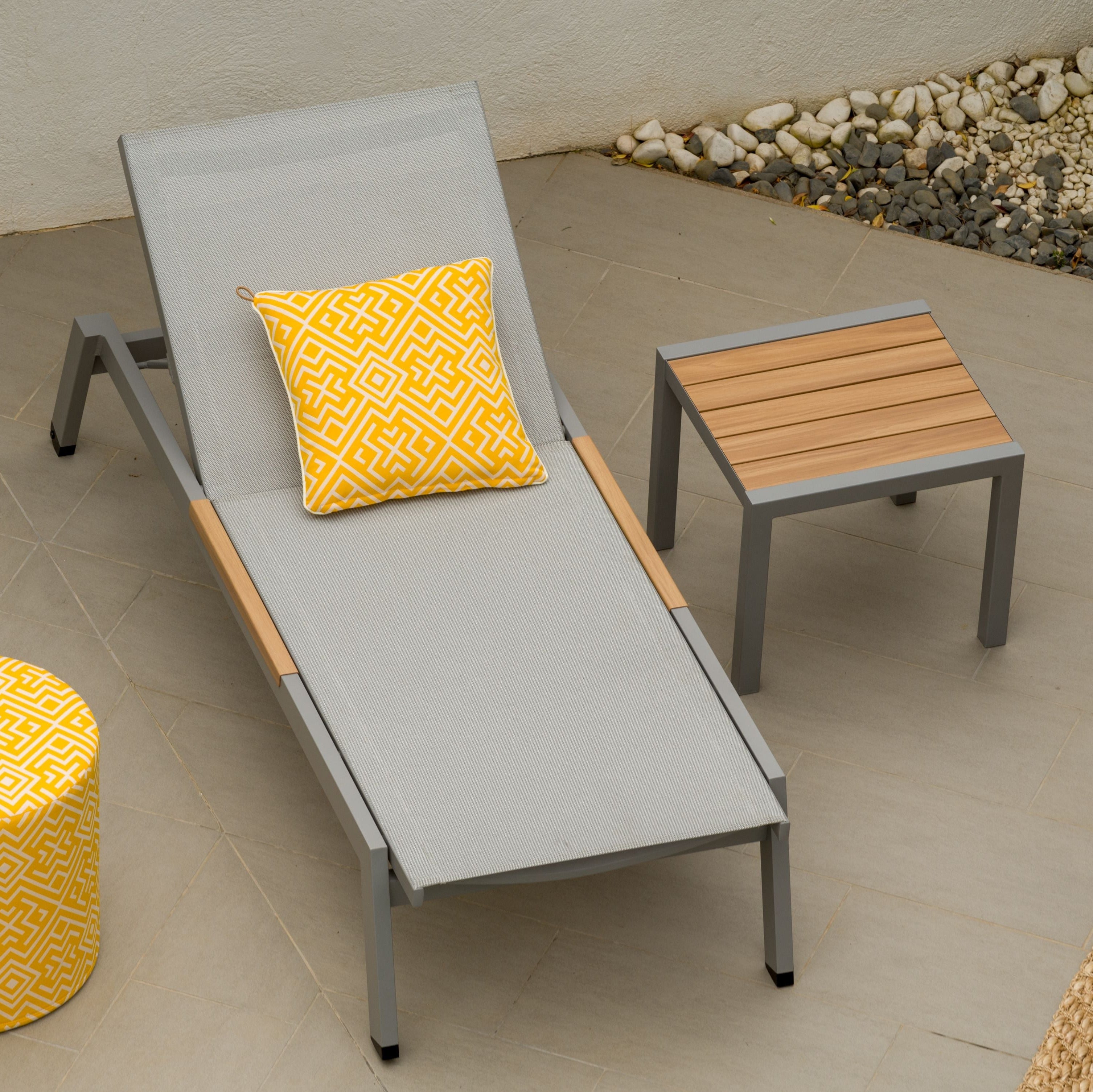 Outdoor furniture set with gray lounge chair, yellow ottoman, and side table on a patio.
