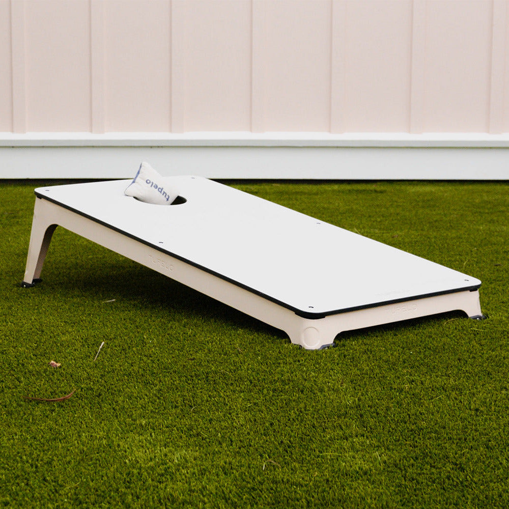 Cornhole board on a grassy area with a light-colored wall in the background
