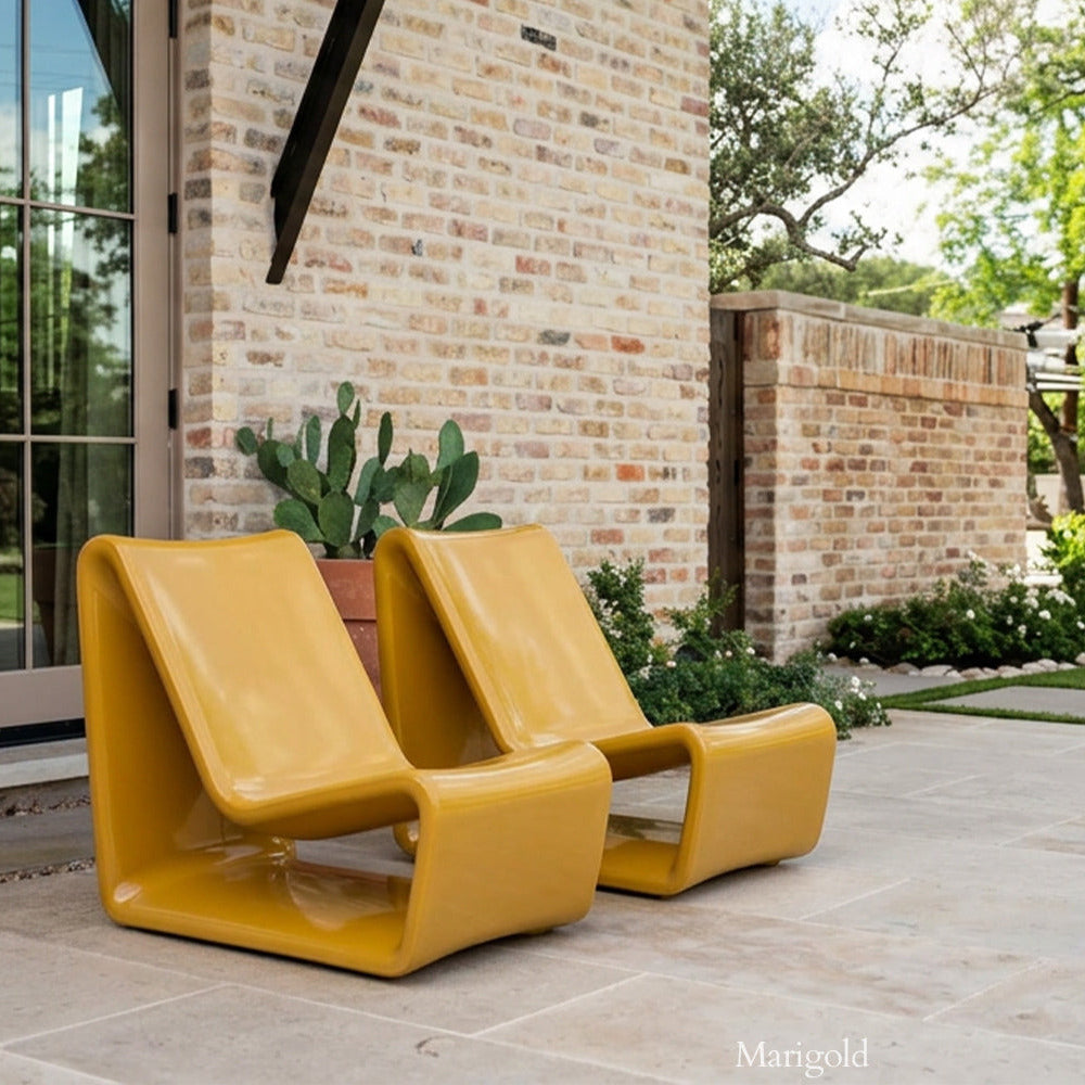 Two yellow modern chairs on a patio with a brick wall and garden in the background.