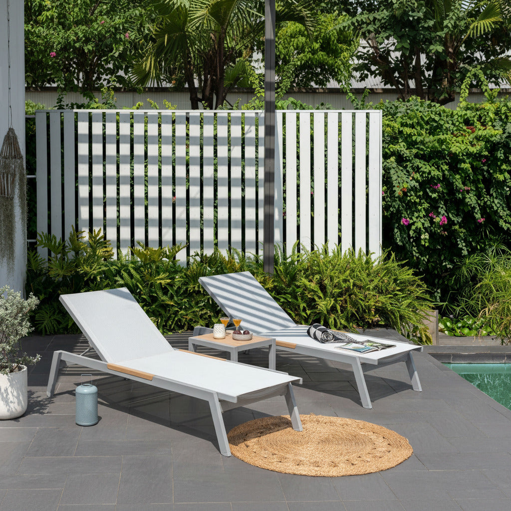 Two white lounge chairs on a patio by a pool with a garden in the background.